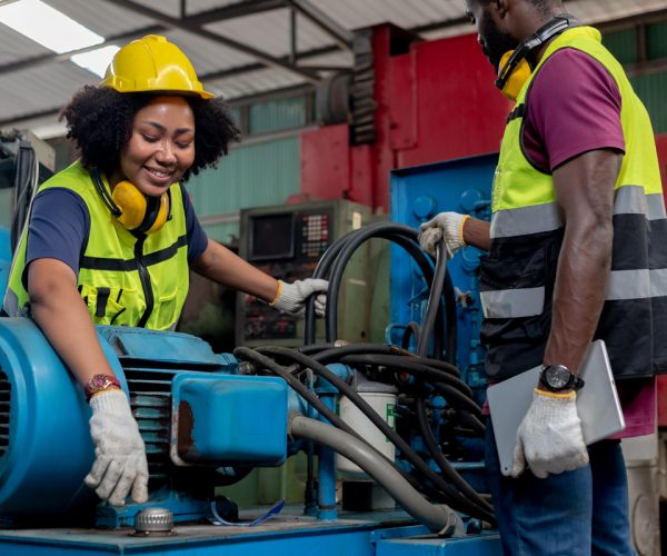 Concept of technician heavy industry, Teamwork African American engineer wear hardhat working at machine in factory. Team technician control metalwork lathe industrial.